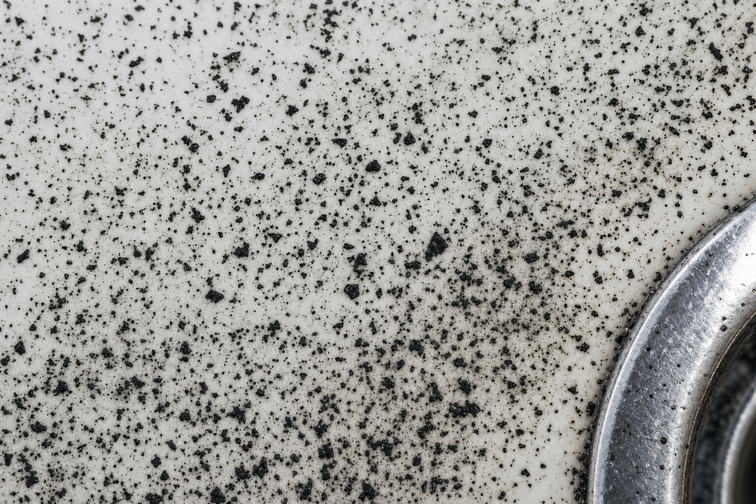 Black manganese specks and dark spots scattered across a white sink basin