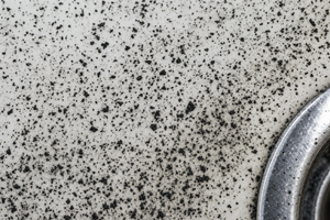 Black manganese specks and dark spots scattered across a white sink basin