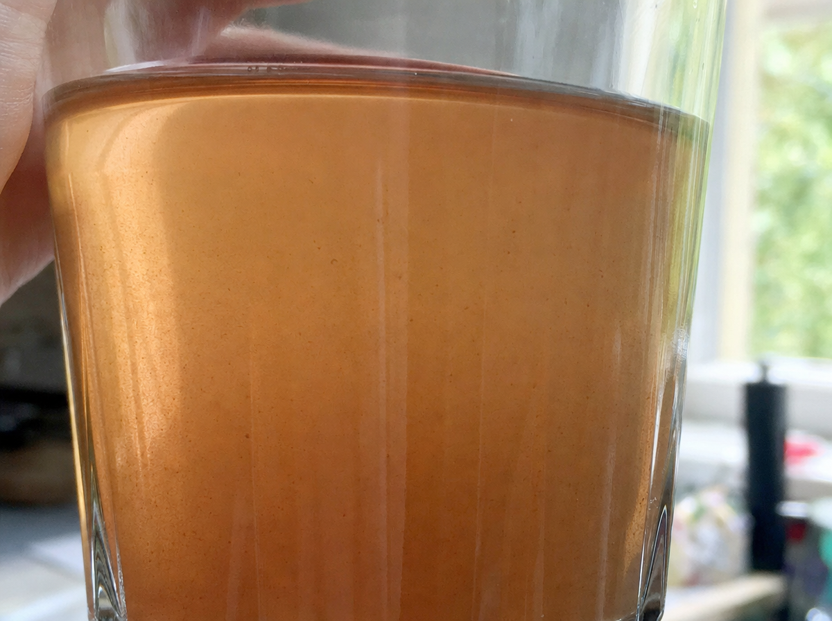 Close-up of a glass of brownish-red iron-contaminated well water held up to kitchen window light